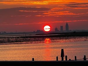 Vibrant red sunset over water with silhouetted structures and posts along the shoreline.