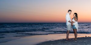 Couple embracing romantically on a sandy beach at sunset with colorful pink and orange sky over the ocean.