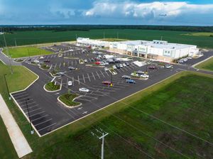 Panoramic aerial view of large commercial development with parking lots and green spaces.