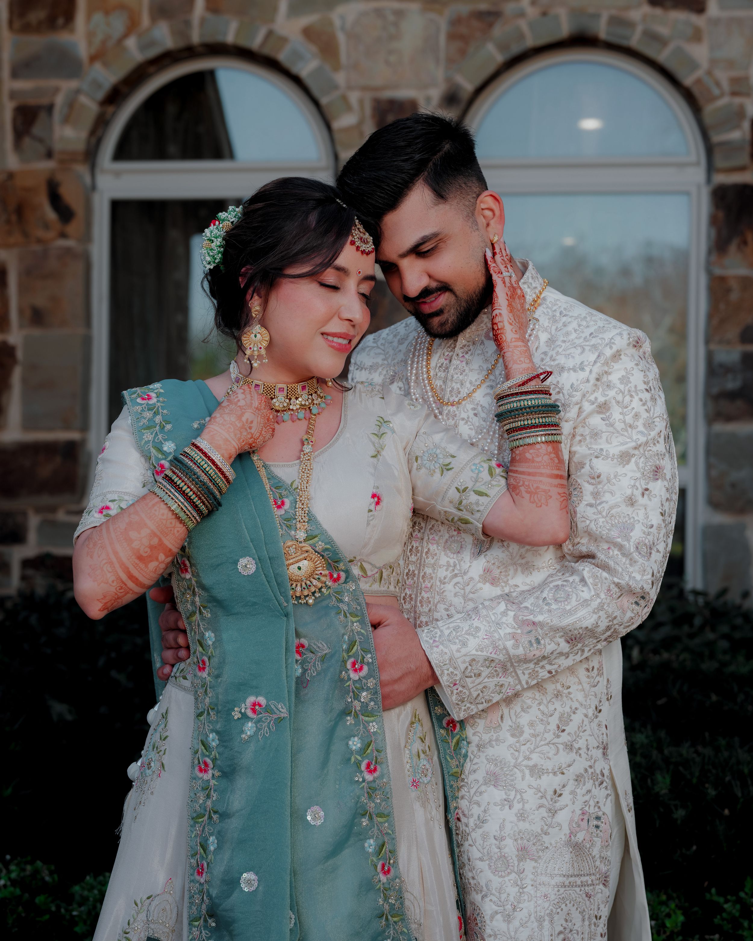 A romantic couple in traditional South Asian wedding attire share intimate moments in an outdoor photoshoot.