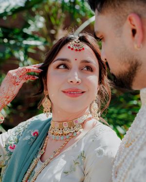 A close-up portrait showing intricate bridal jewelry and henna details in an outdoor garden setting.
