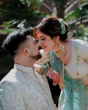 A romantic couple in traditional Indian wedding attire share intimate moments in a garden setting.