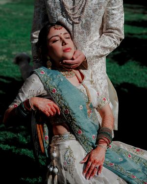 Artistic wedding photo showcasing detailed embroidery and jewelry against a sunlit garden background.