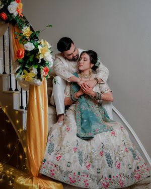 Couple in ornate period costumes with floral embroidery dance together against gold and floral decorations.