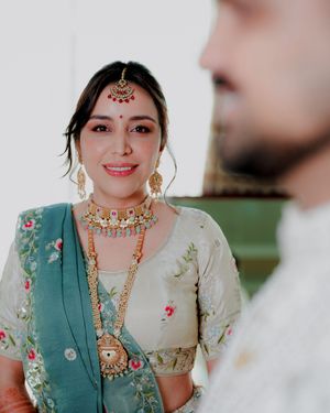 Traditional Indian wedding attire featuring ornate jewelry and embroidered teal and cream colored outfits.