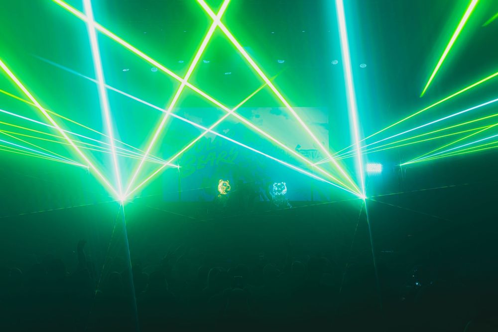 Vibrant green laser beams illuminate a dark concert venue creating a dynamic geometric light show effect.