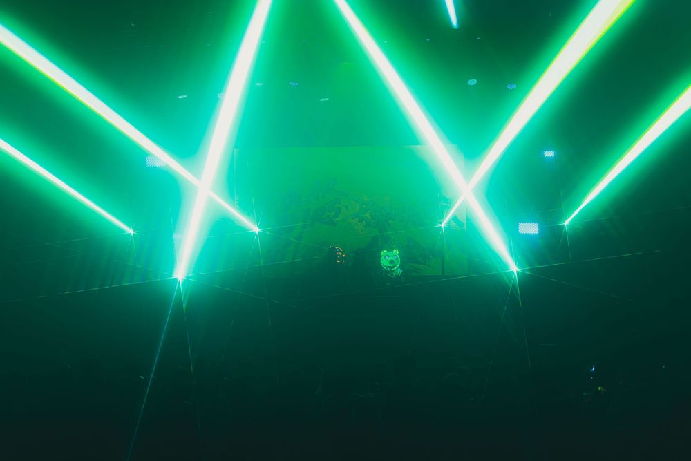 Green neon lights create geometric patterns against a dark background in a nightclub or event space.