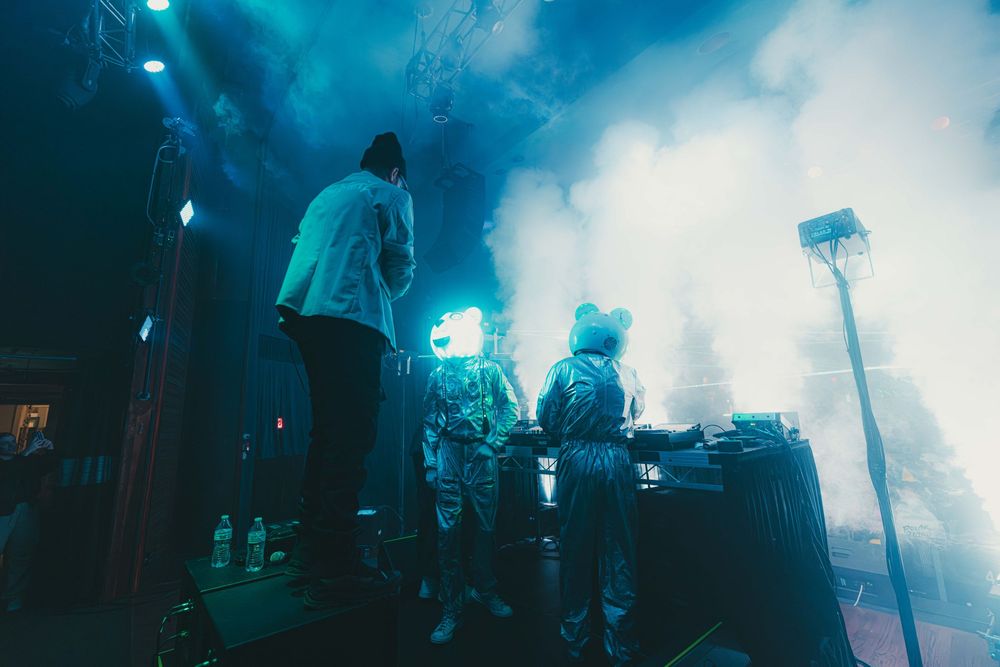 Silhouetted figures perform on a misty concert stage with blue atmospheric lighting and fog effects.