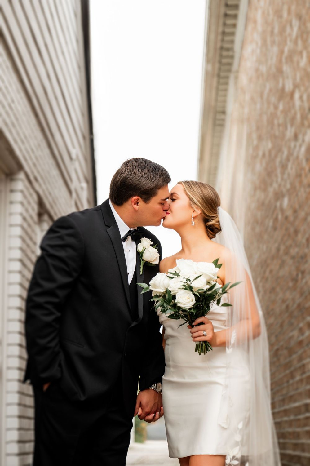 A romantic wedding moment captured between brick walls as the couple shares a kiss.