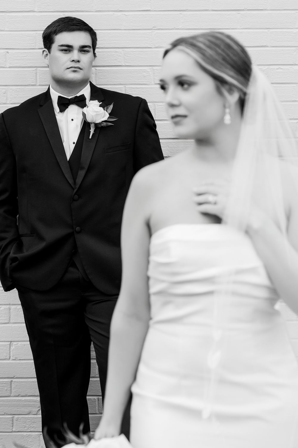 Black and white portrait of newlyweds posing against a white wall.