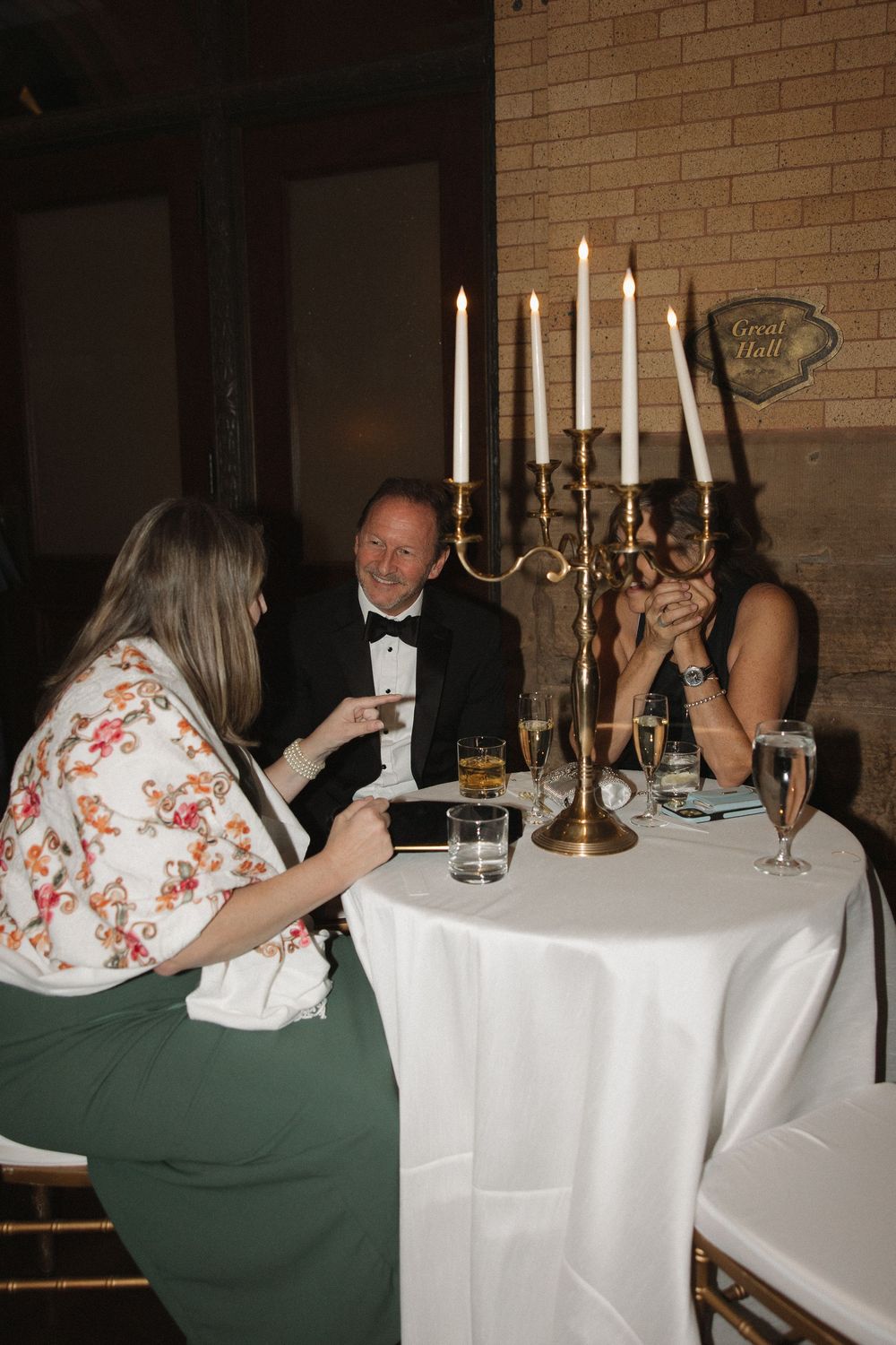 Elegant dinner table setting with white tablecloth, candelabras, and guests seated in a brick-walled restaurant.