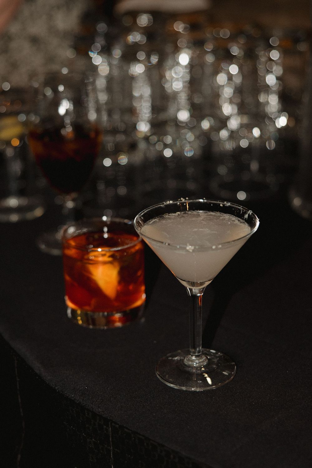 Two elegant cocktails on a dark bar counter with blurred glassware in the background.