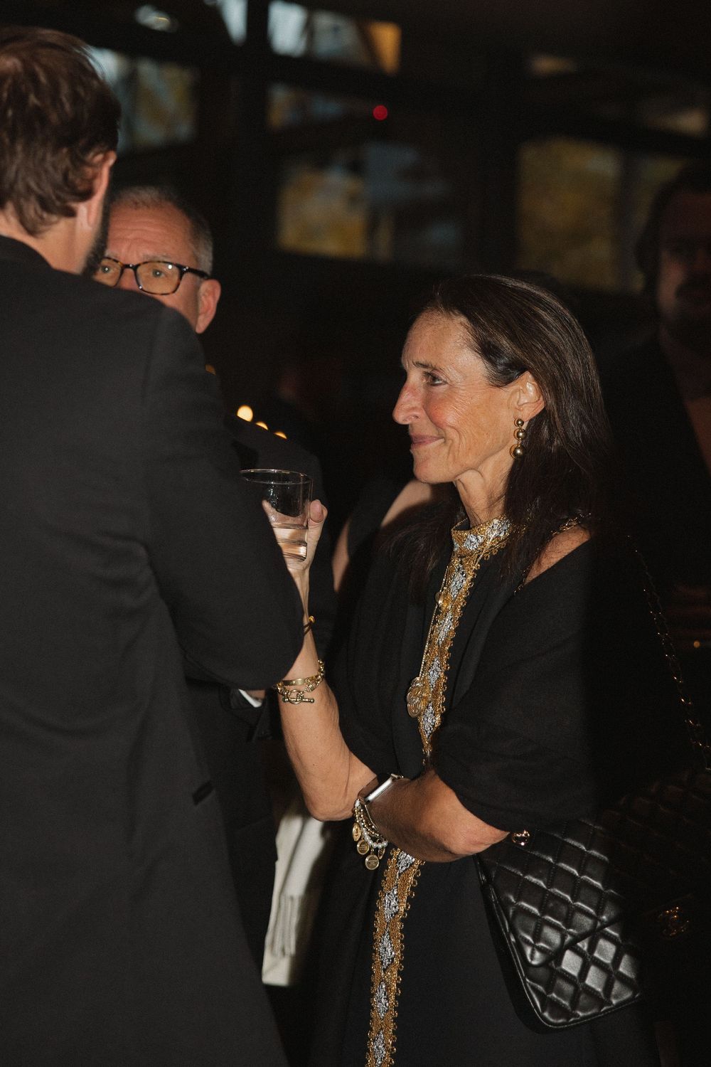 Guests in formal attire mingle at an elegant evening event with dim lighting and cocktails.