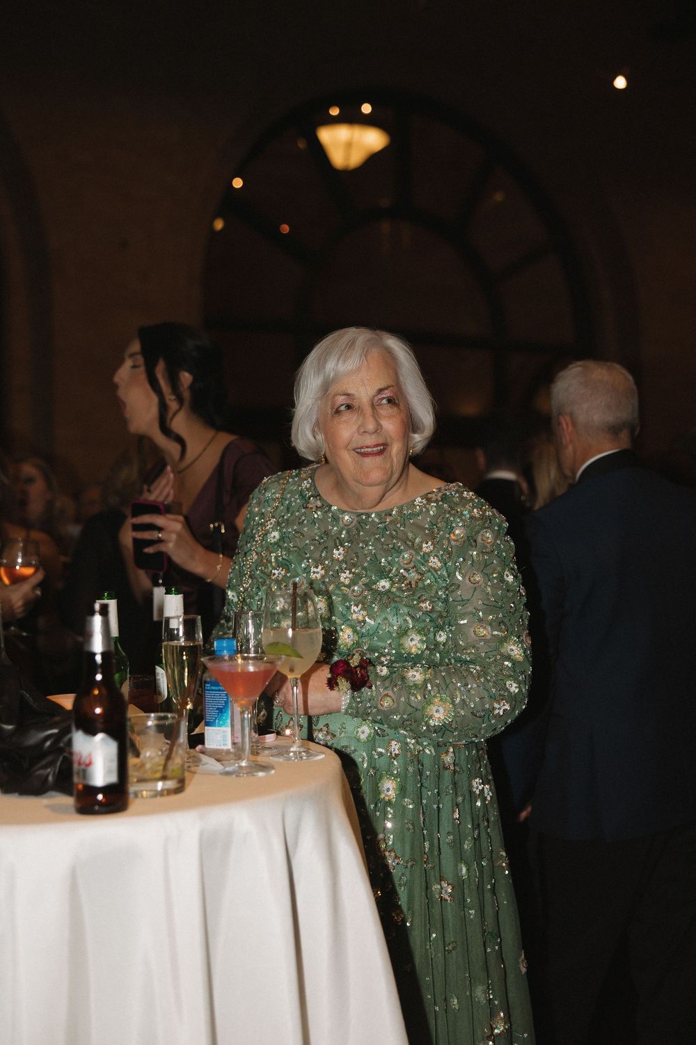 Woman in sparkly green evening gown stands near white-clothed tables at a formal event.