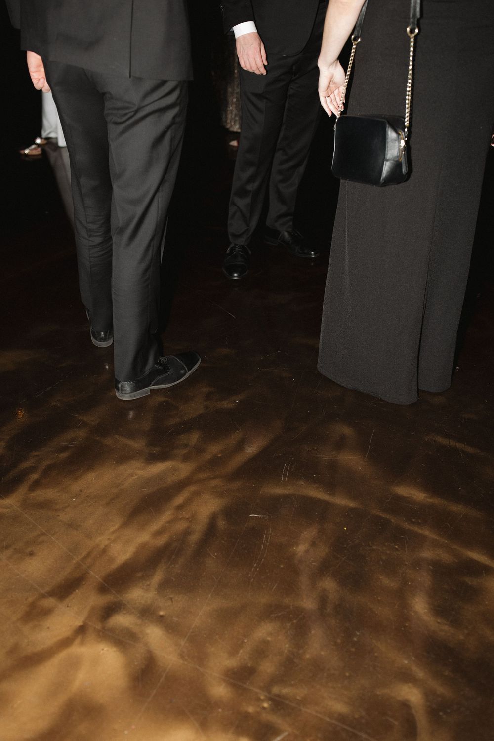 Hardwood dance floor with multiple people's feet visible in formal black attire at an elegant event.