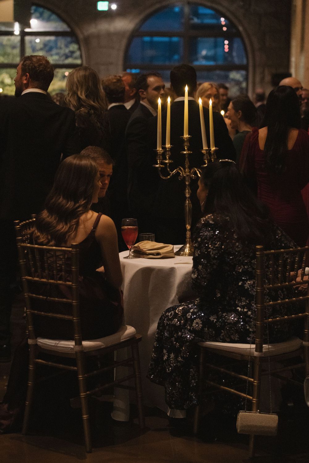 Elegant dinner party setting with gold chairs and candlelit tables in a dimly lit venue.