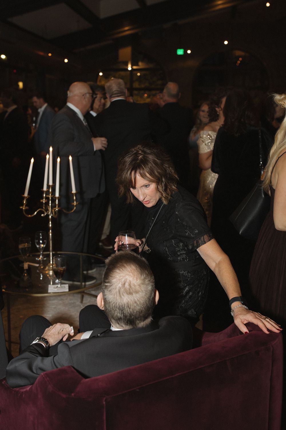 People gathered at a dimly lit event space with burgundy seating and candles on tables in the background.