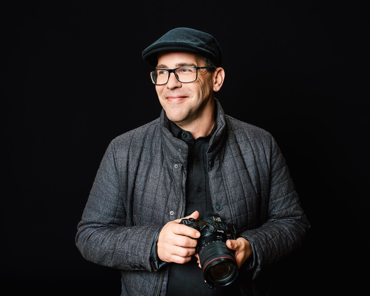 An event photographer in a gray coat and black cap poses with a camera against a dark background in multiple artistic shots.