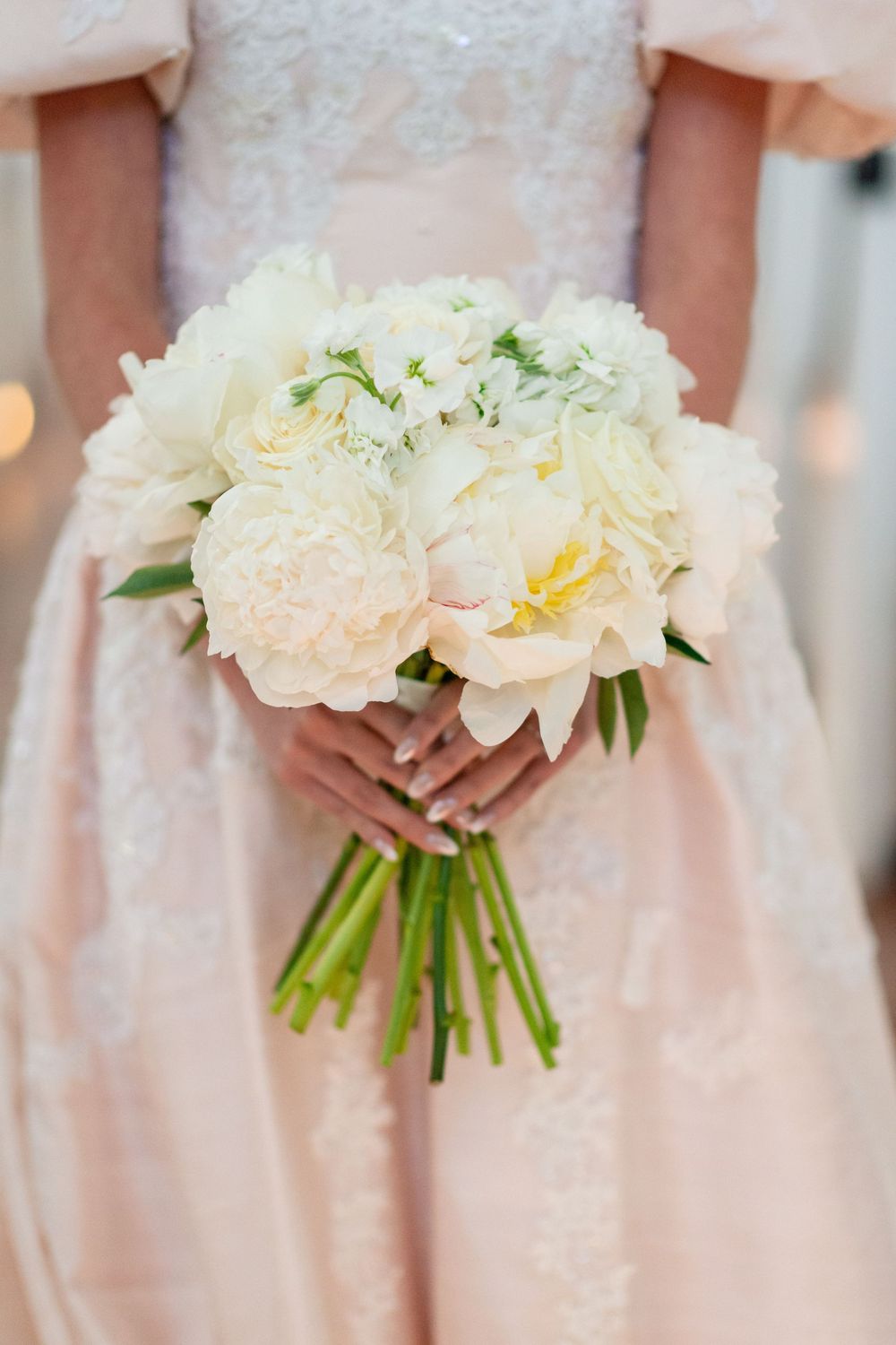Row of bridesmaids holding elegant white peony bouquets in soft pink dresses.