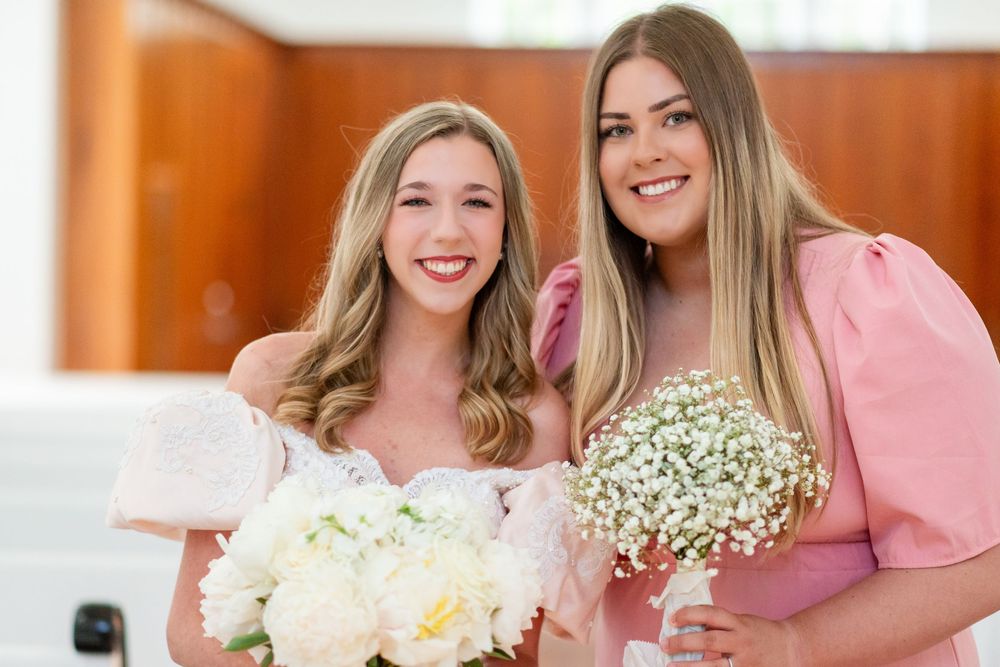 Bridesmaids in pink dresses hold white floral bouquets while posing together in an elegant indoor setting.