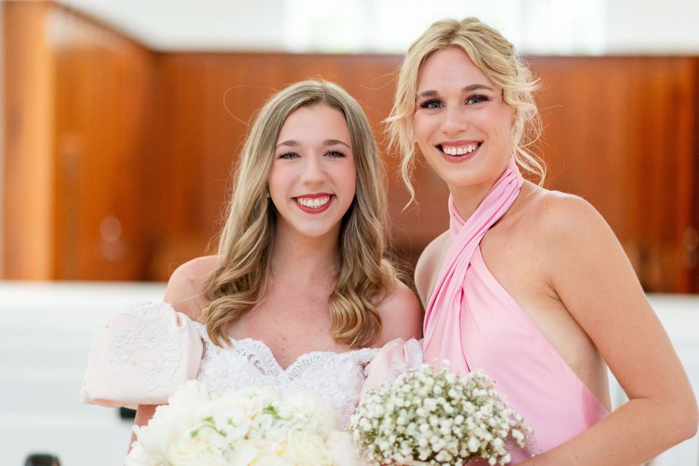 Wedding party members pose with bouquets in a church setting.