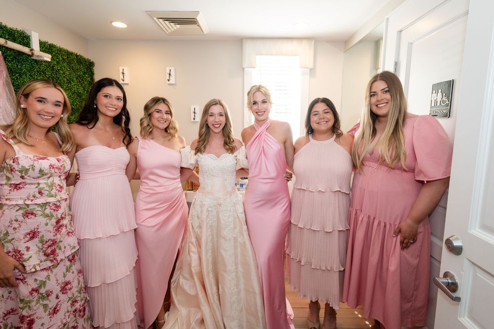 Bridal party in pink dresses posing together in a bright indoor setting.