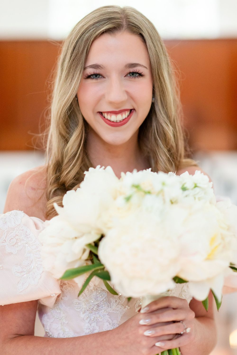A radiant bride in a white dress holds a bouquet of white peonies.