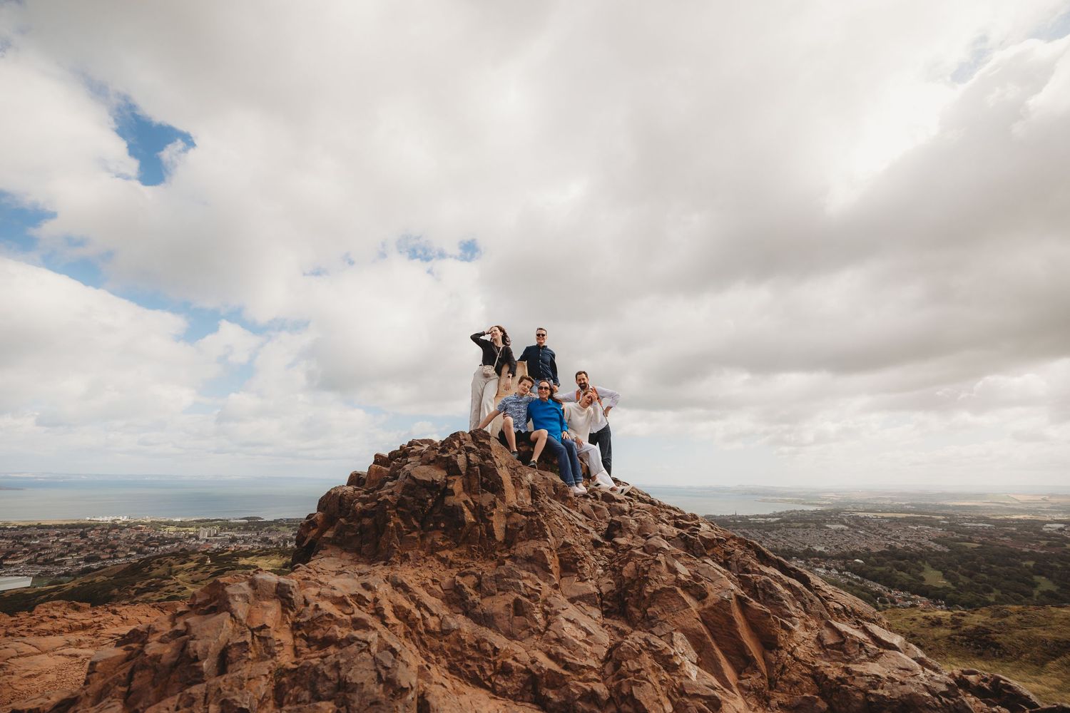 Adventurous hikers stand atop a rocky outcrop overlooking a vast desert landscape under cloudy skies.