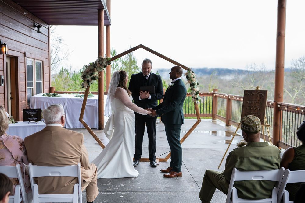 An intimate outdoor wedding ceremony takes place on a covered deck with mountain views in the background.