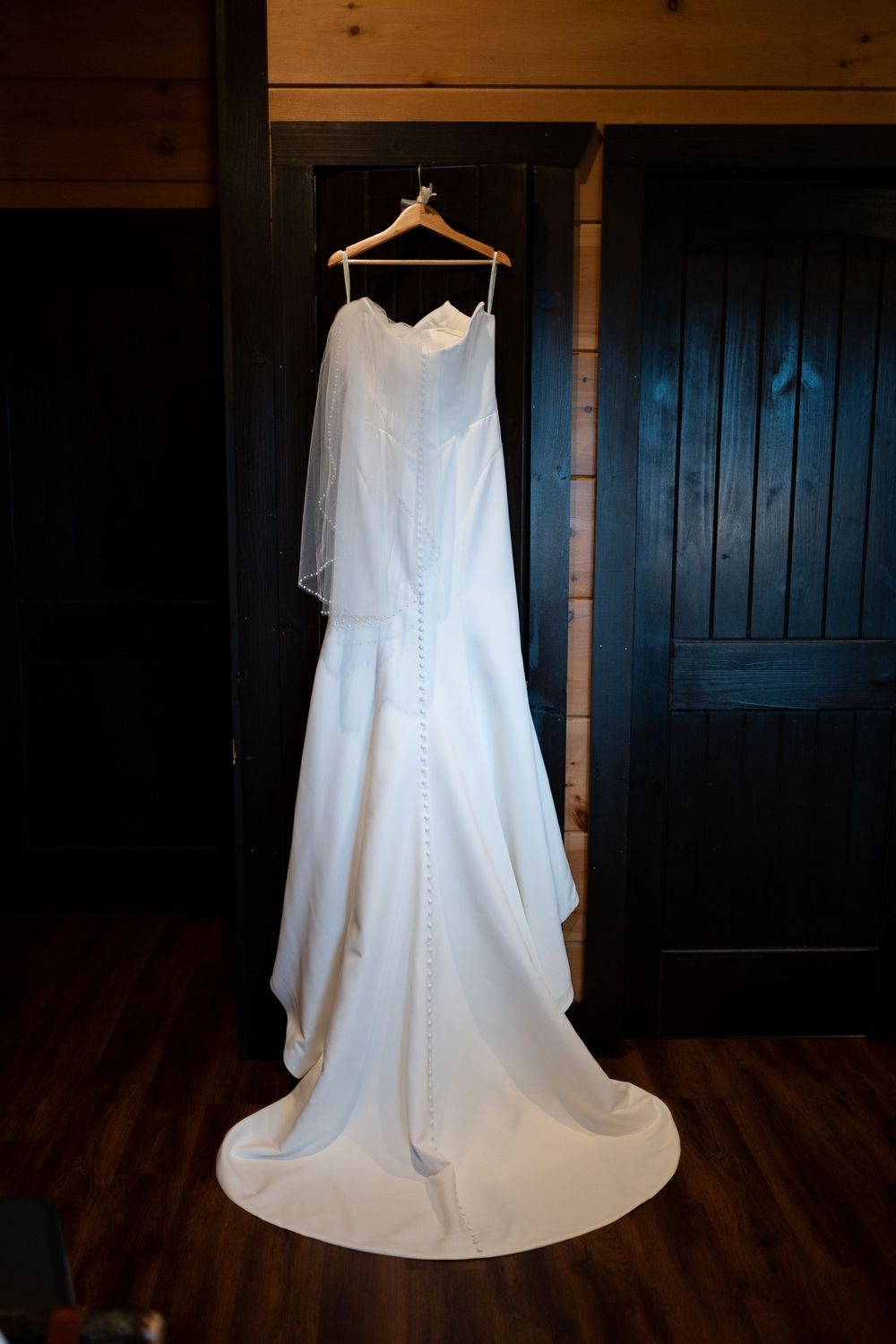 White wedding dress hanging elegantly against dark wooden walls in dramatic lighting.
