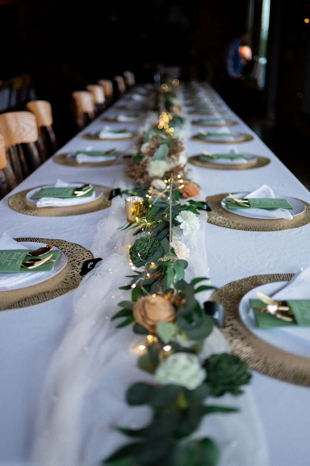 Elegant table setting with white linens, greenery garland, and gold charger plates for an upscale wedding reception.