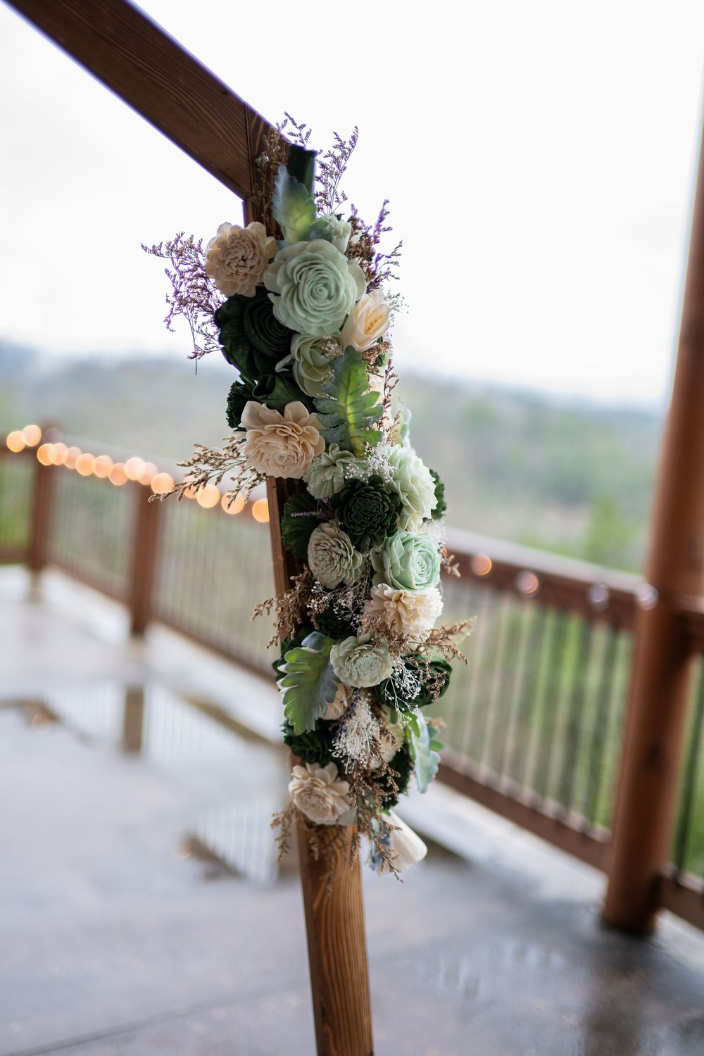 Rustic wooden post decorated with delicate white and mint green floral arrangements on an outdoor deck.