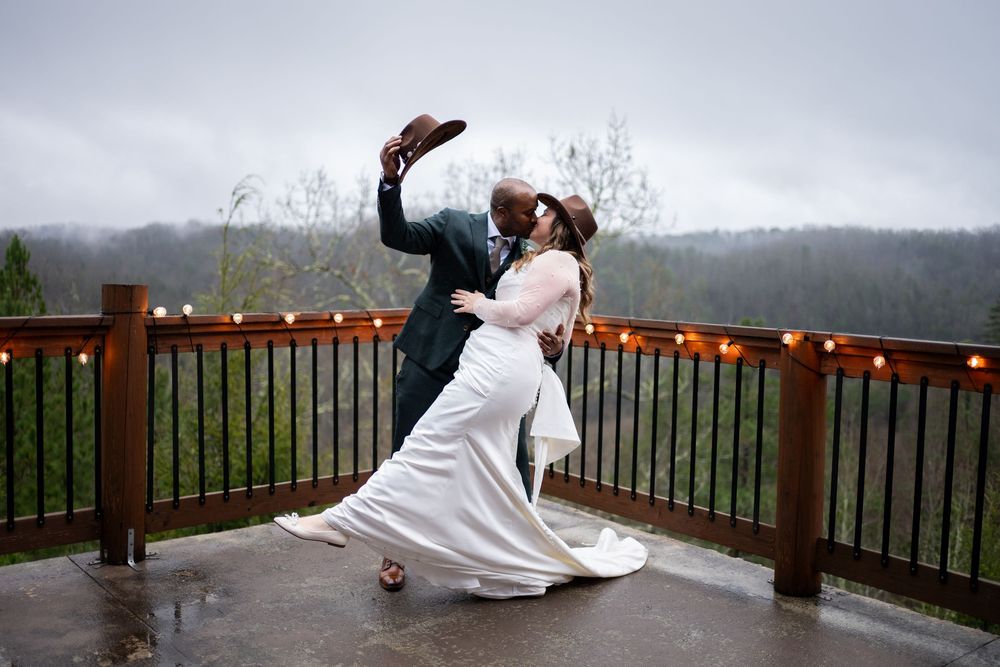 Wedding couple dancing playfully on a covered outdoor deck with mountain views in the background.