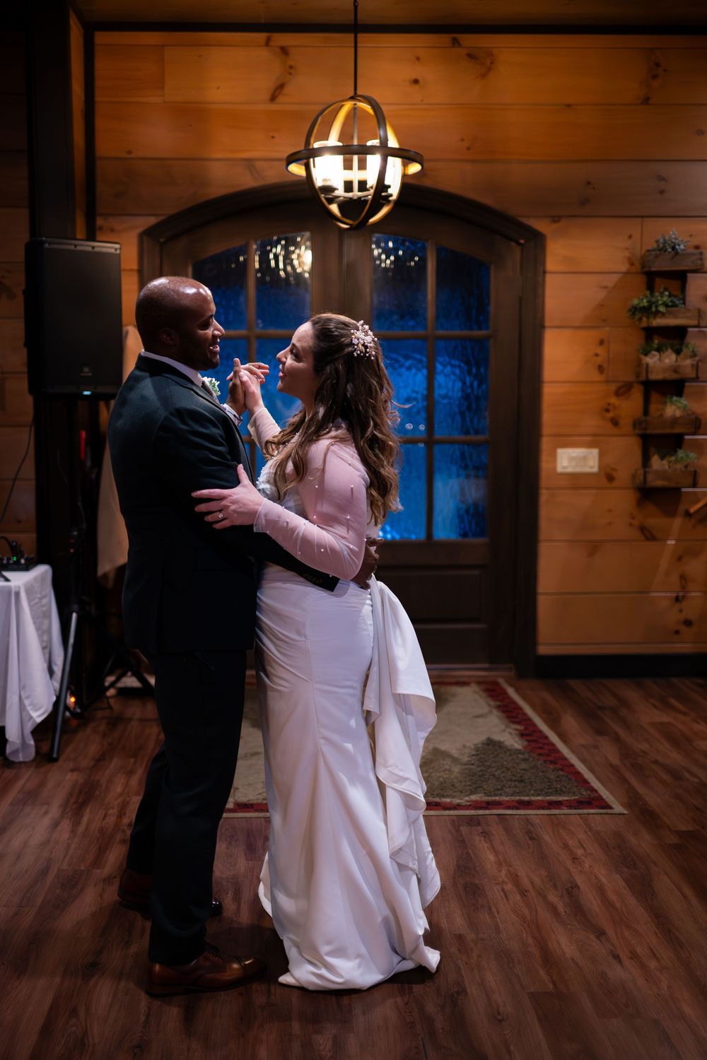 A couple shares a romantic dance together in a rustic wooden cabin venue with warm lighting and hardwood floors.