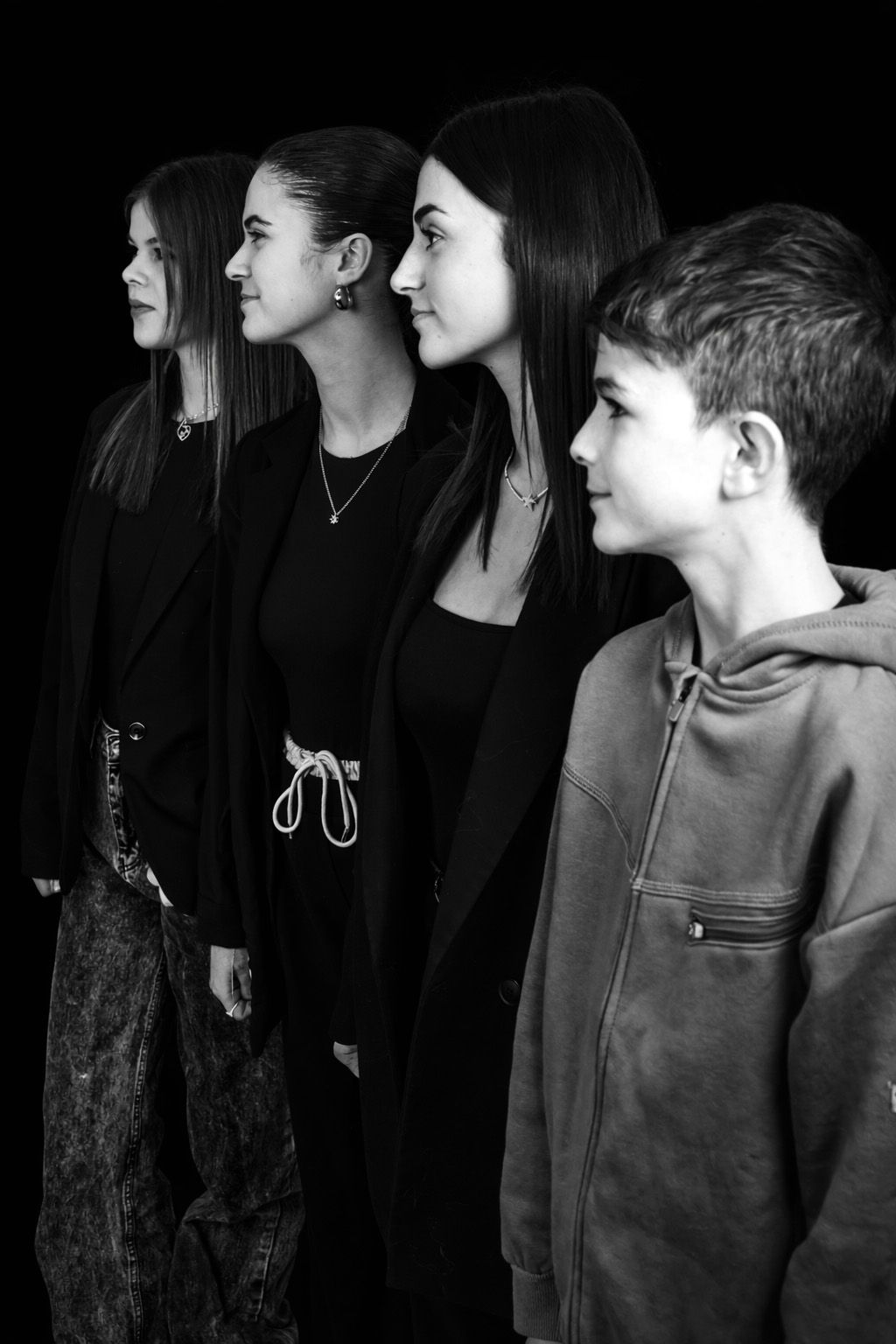 A series of black and white profile portraits showing people in dark clothing arranged in a line against a black background.