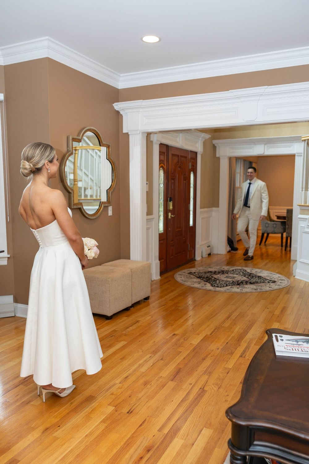 Interior view of a room with hardwood floors, white trim, and tan walls showing a figure in a white dress.