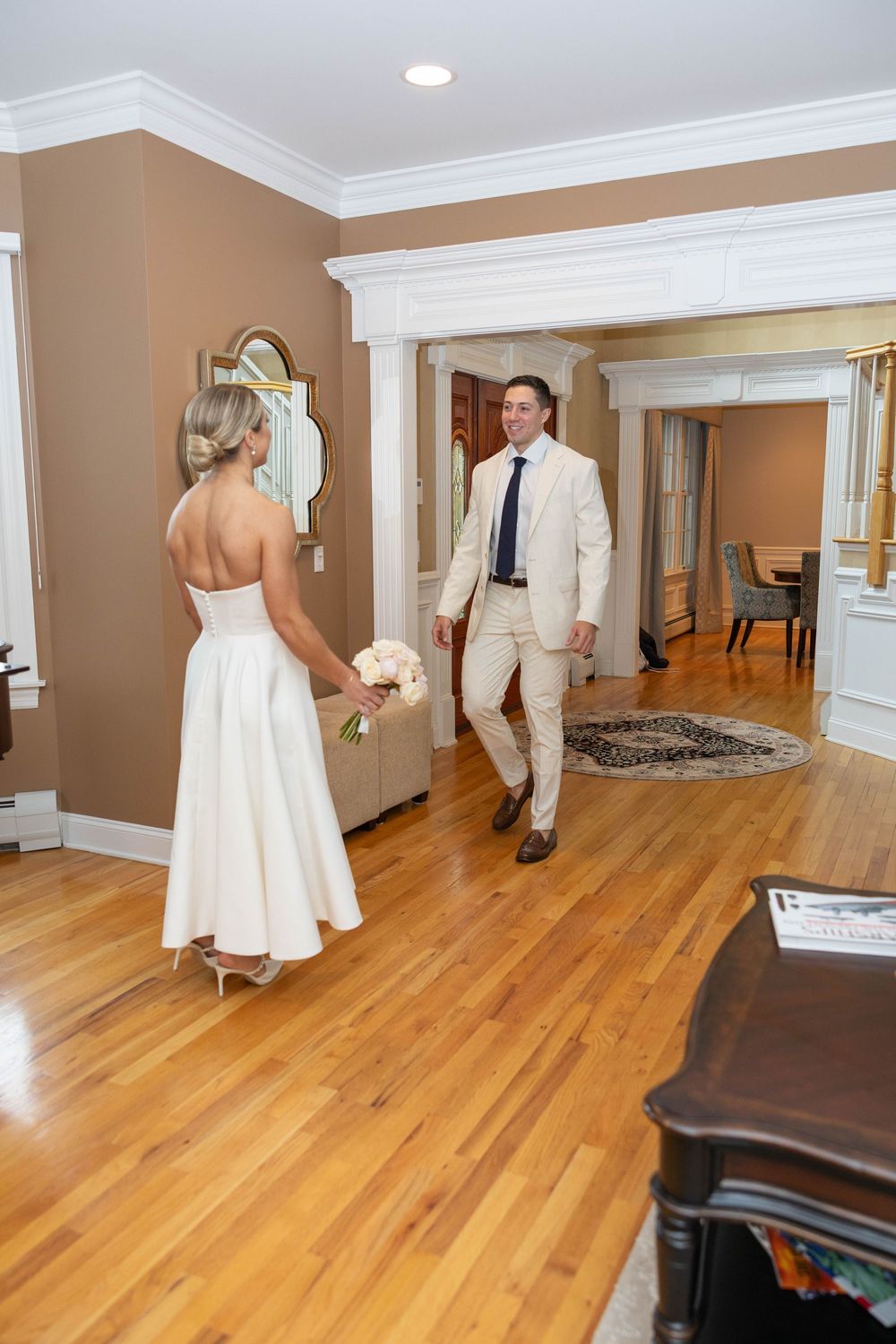 A wedding first look moment captured in a series of photos showing the couple meeting in an elegant room with hardwood floors.