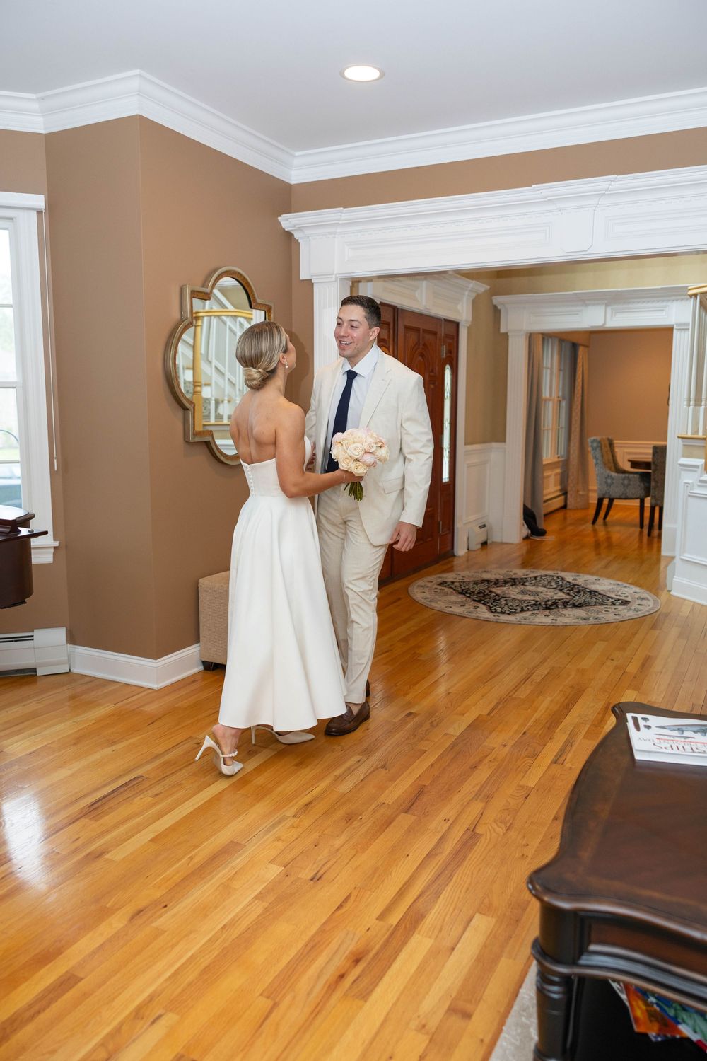 Bride and groom share a quiet moment in an elegant room with hardwood floors and tan walls during their wedding day.