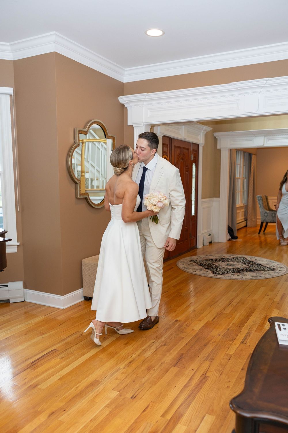 Newlywed couple dancing together on hardwood floors in an elegant room with white trim and beige walls.