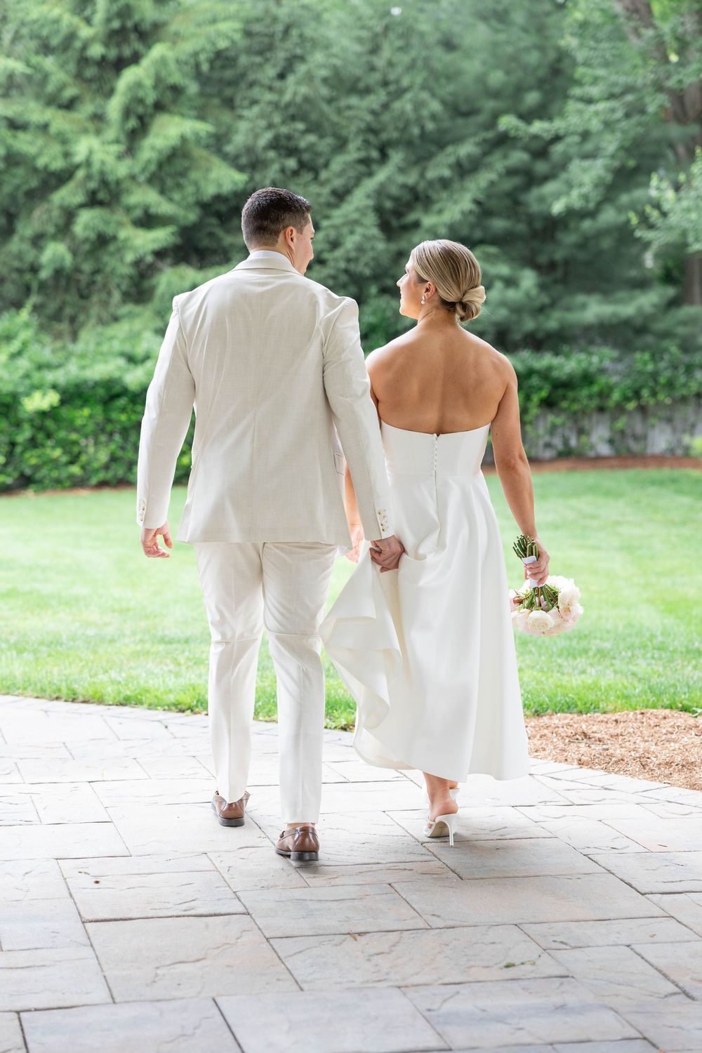 A couple in white attire sits together on stone steps in a lush garden setting.