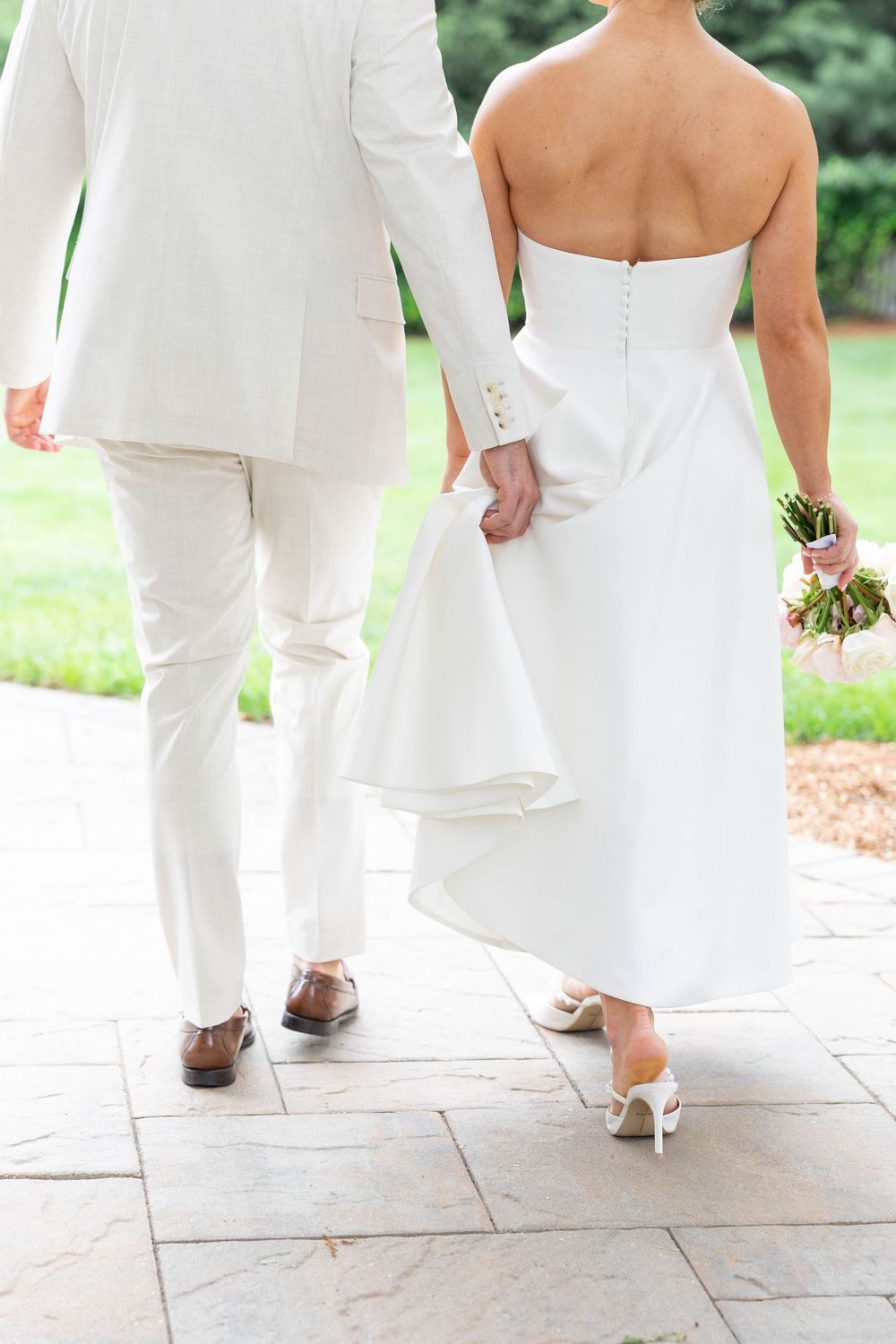 A group wearing all white formal attire walks together on a stone patio showing only their lower halves and shoes.