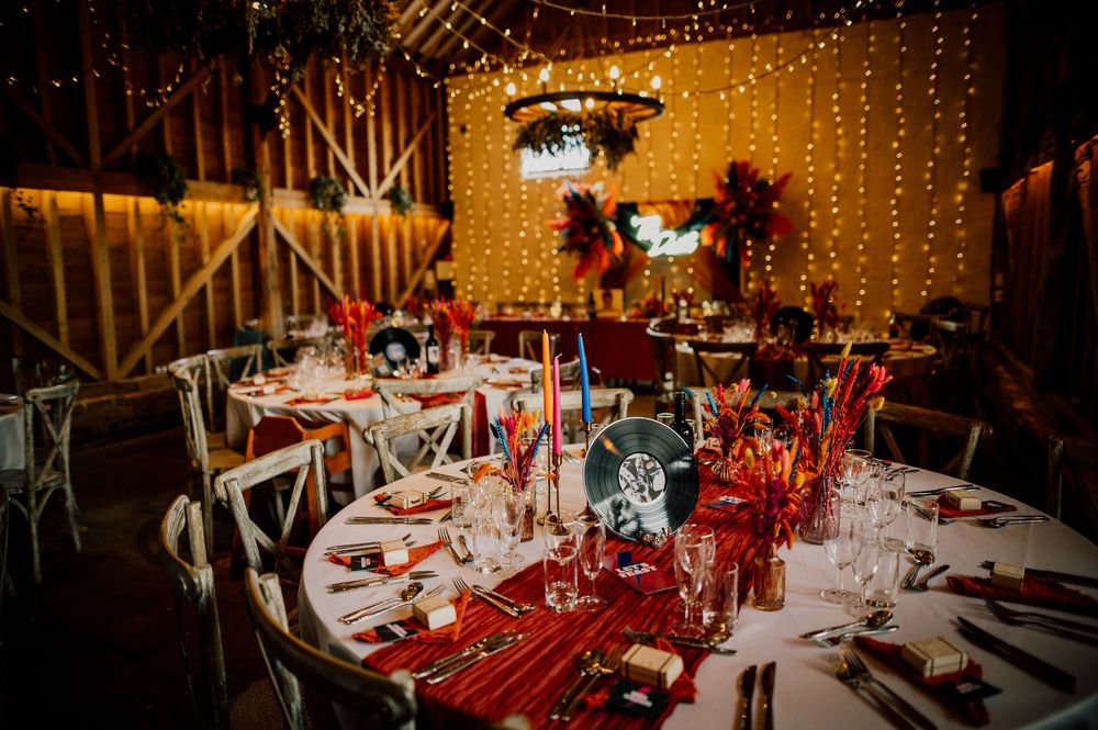 Elegant wedding reception tables decorated with red accents, white linens, and twinkling string lights in rustic barn setting. Worcestershir