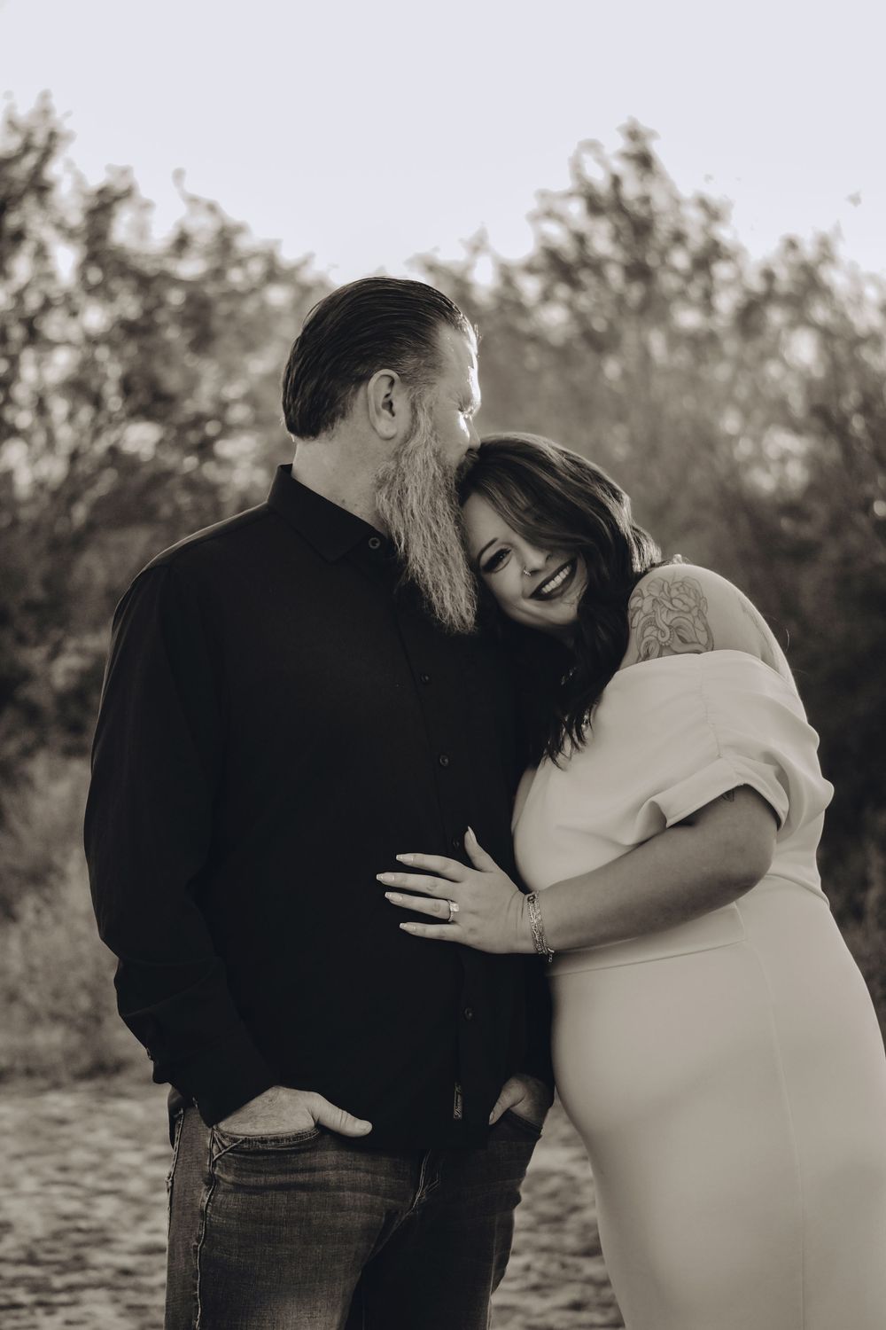 A couple embraces in a romantic black and white photo series by a lake at sunset.