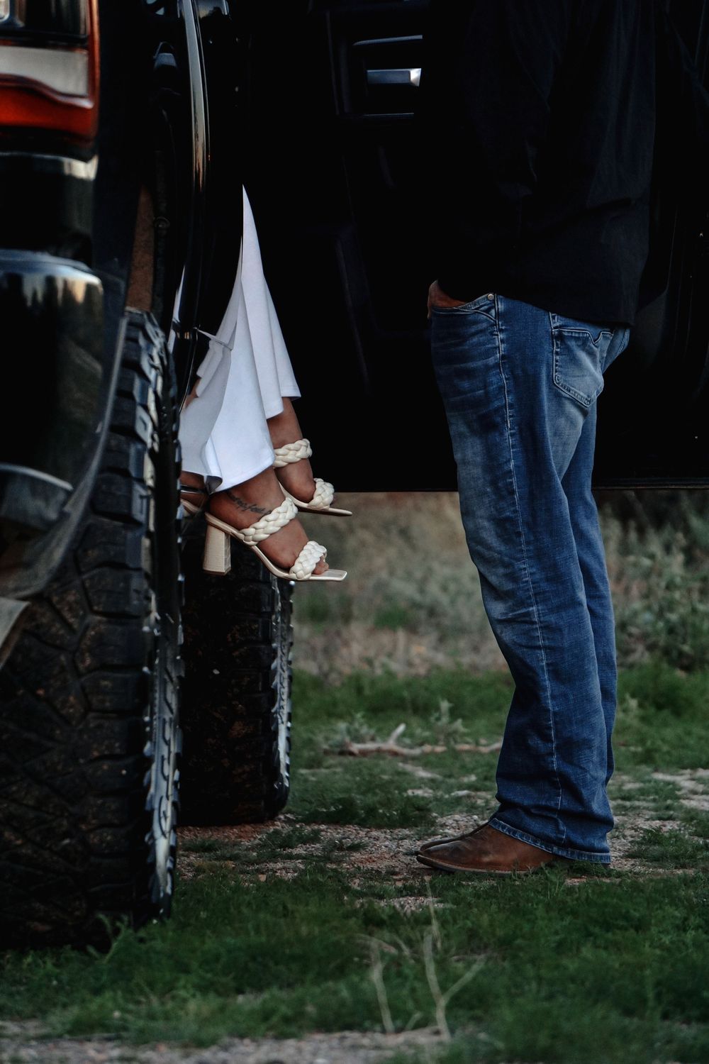 Several people in jeans and casual shoes stand on grass in a line formation.