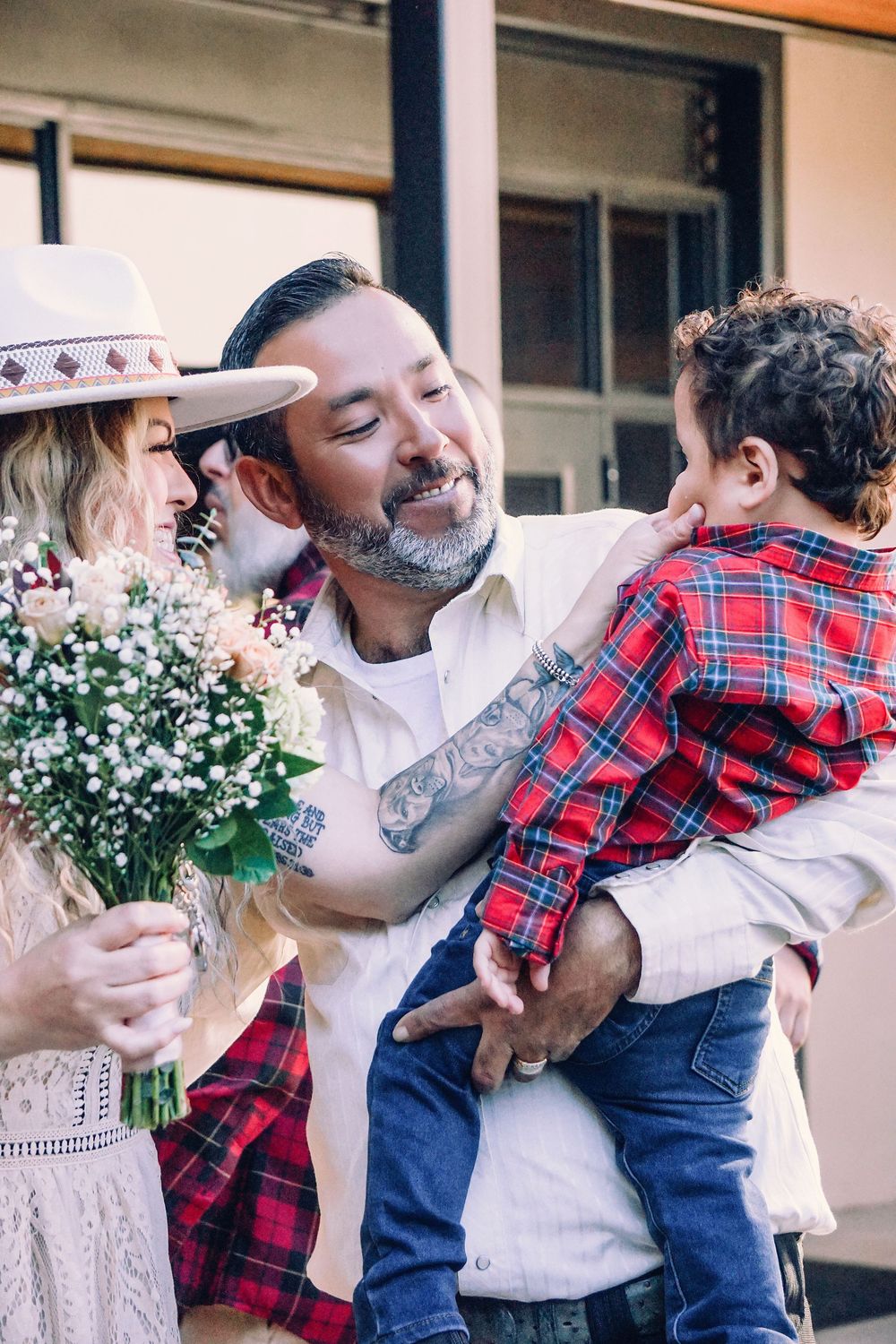 A heartwarming family moment captured showing embraces and white flowers against a building exterior.