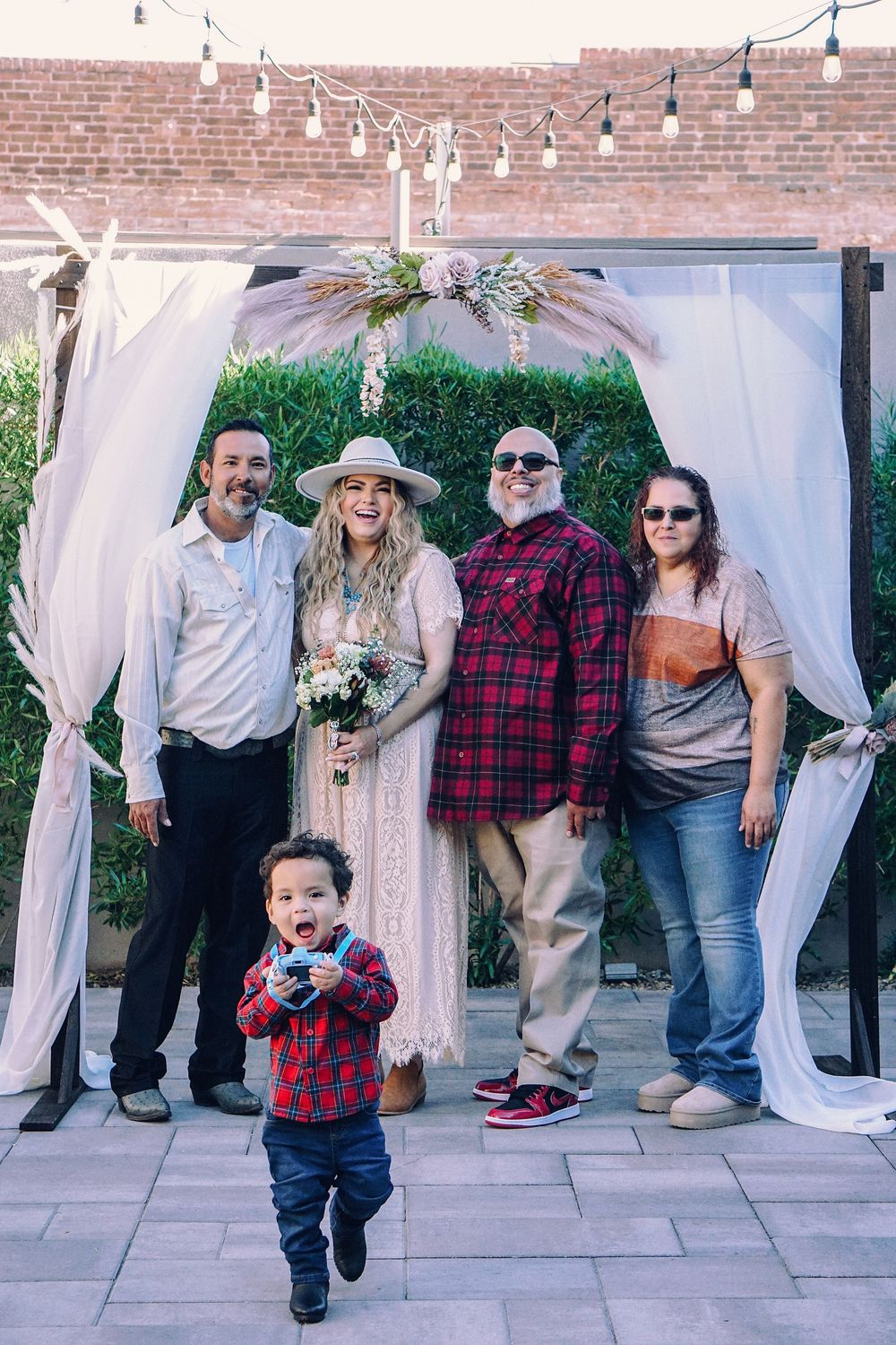Family gathering outdoors with white curtains and brick wall backdrop during a celebration.