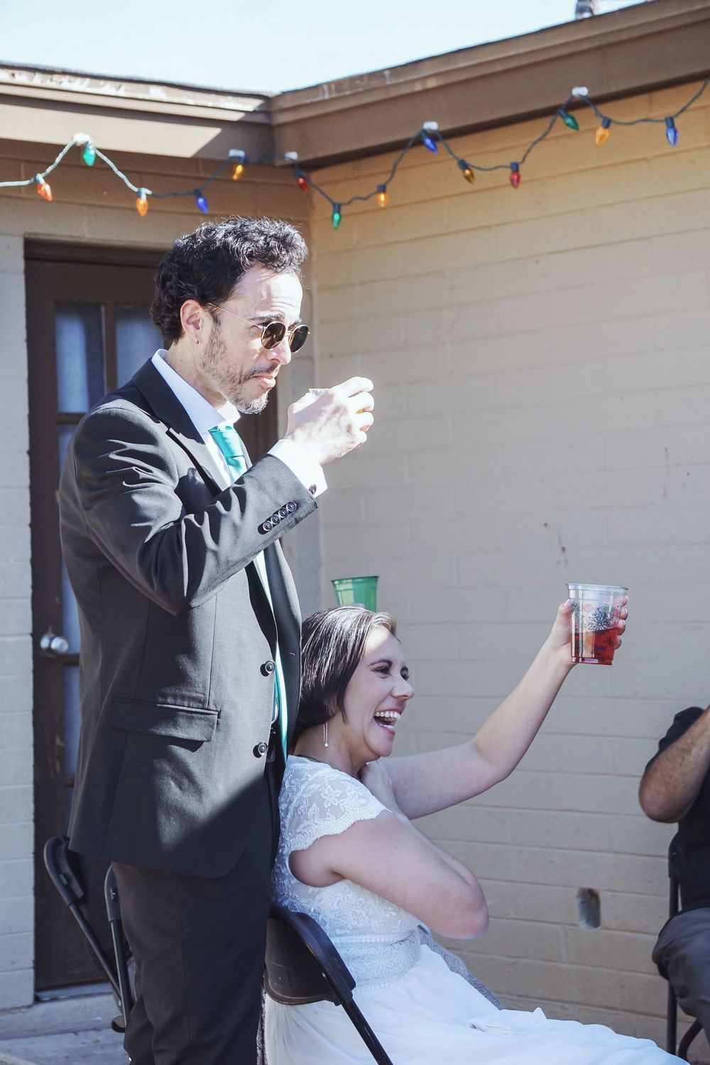 Wedding guests dance and celebrate together under colorful string lights at an outdoor reception.
