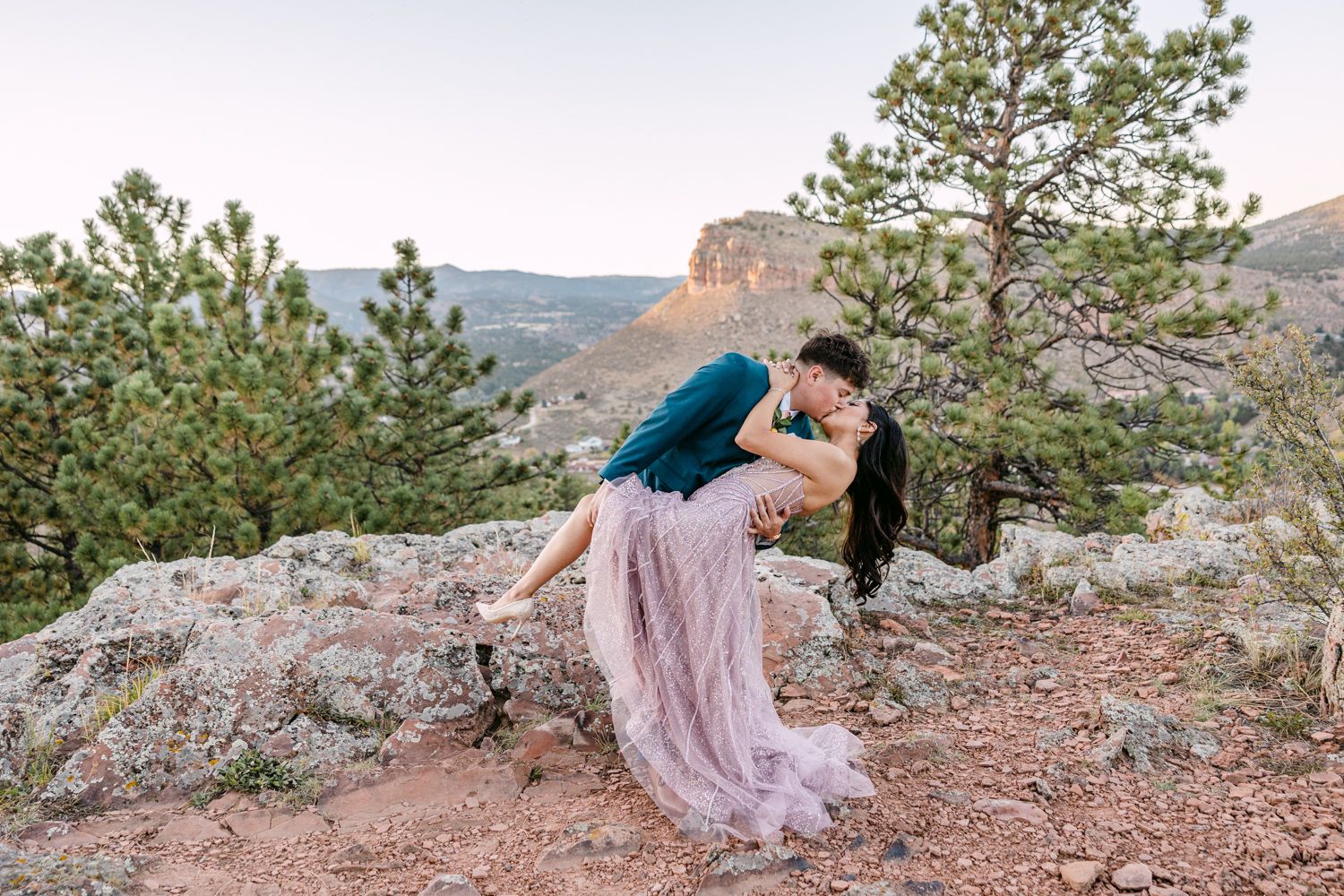A couple stands together on a rocky mountain overlook during sunset in Colorado.