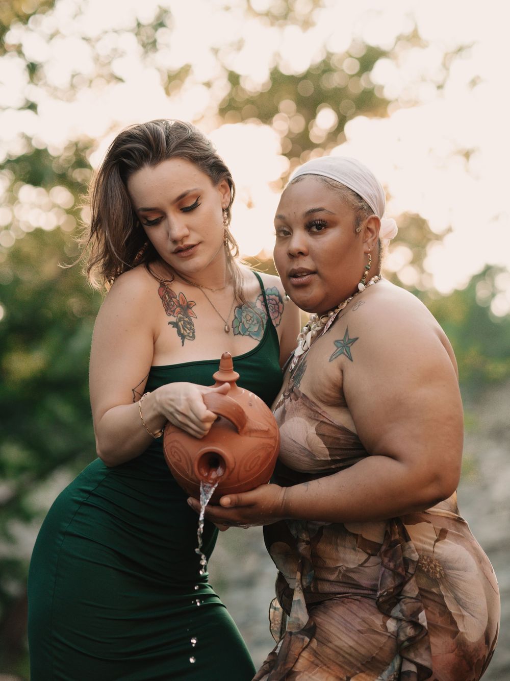 Two women standing in the Vermilion river pouring water from a terracotta colored vase
