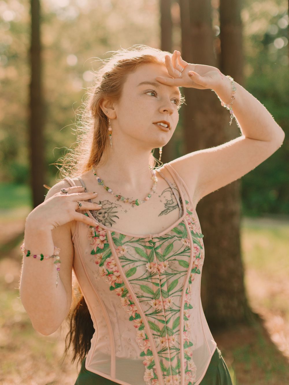Witchy woman in a sunlit forest wearing a dark velvet cloak holding a hand to her cheek